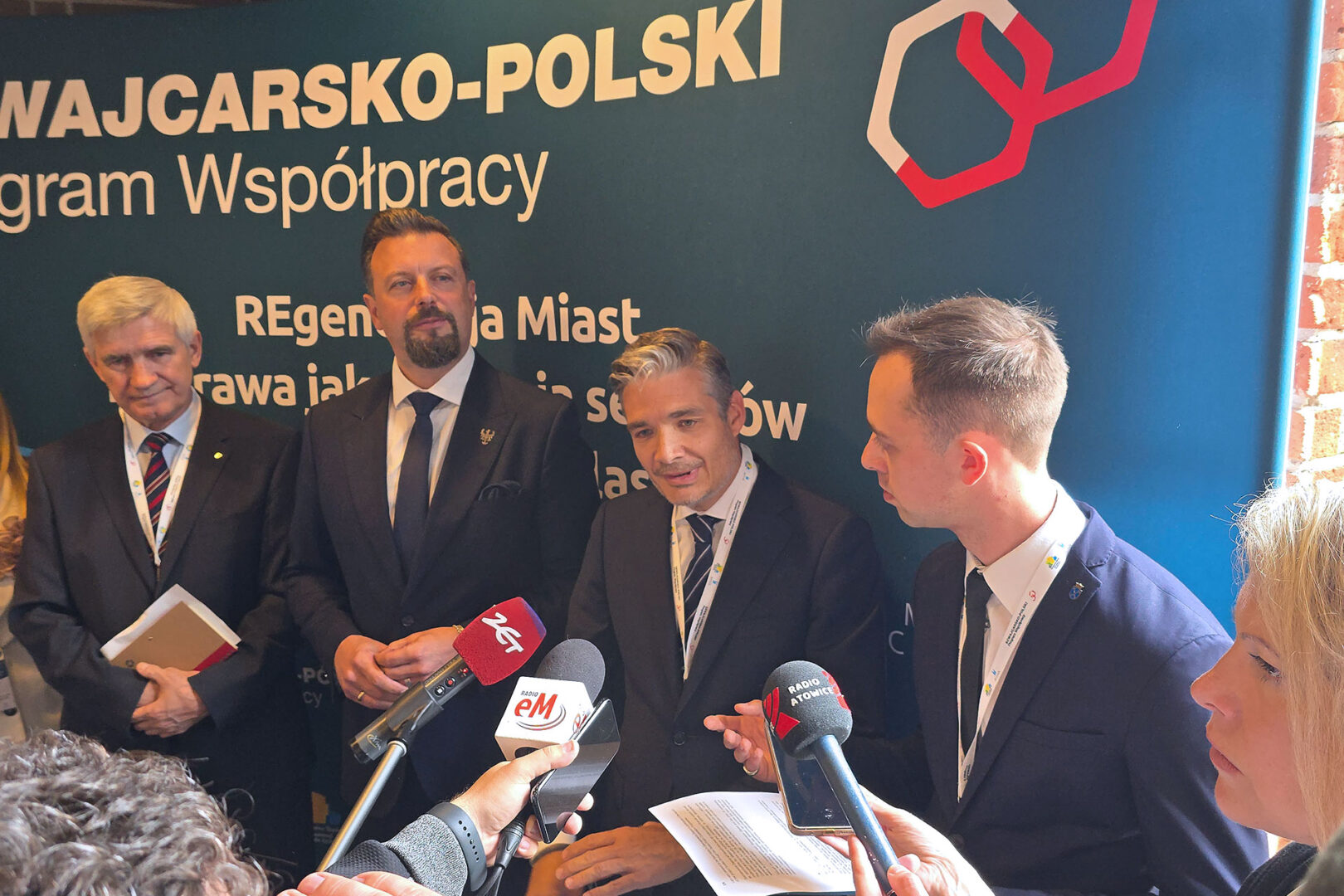 Lokalny polityk udziela wywiadu na tle ścianki Szwajcarsko-Polskiego Programu Współpracy. Obok niego stoi trzech innych polityków.